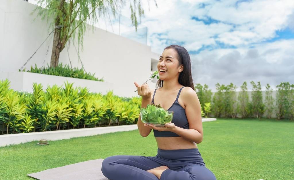 A happy woman eats a green salad outdoors to improve digestion naturally.